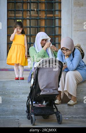 Türkische Frauen mit einem Kind, die auf den Stufen der Blauen Moschee in Istanbul, Türkei, sitzen Stockfoto