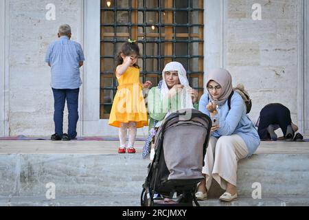 Türkische Frauen mit einem Kind, die auf den Stufen der Blauen Moschee in Istanbul, Türkei, sitzen Stockfoto