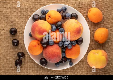 Frische süße Früchte auf weißer Keramikplatte auf Jutetuch, Makro, Draufsicht. Stockfoto