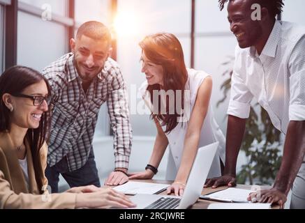 Glückliche junge Mitarbeiterin, die über ein Online-Projekt spricht und eine Präsentation mit Brille an erfahrene Teamleiterin zeigt. Stockfoto