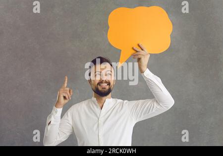 Aufgeregter Mann, der eine Idee hat, eine Sprechblase über grauem Hintergrund zu halten Stockfoto