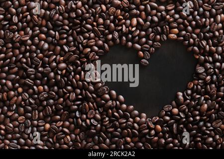 Kaffeebohnen werden in Form eines Herzens auf einer dunklen Holzoberfläche ausgelegt. Draufsicht. Geröstete Kaffeebohnen, Kopierraum Stockfoto