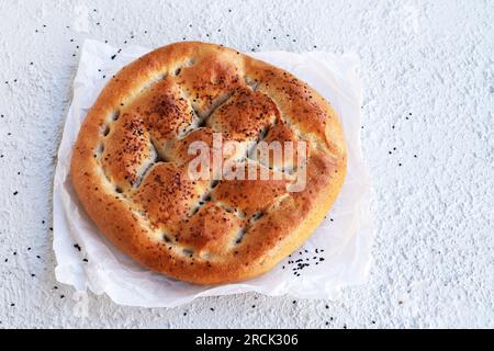 Traditionelles türkisches Ramadan-Brot mit Backpapier auf weißem, strukturiertem Hintergrund, Blick von oben Stockfoto