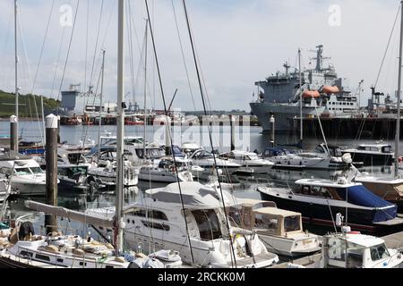 Lokale Segelboote, die im Hafen von Falmouth vor Anker liegen, mit Royal Navy-Schiffen in der Nähe. Stockfoto