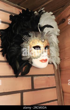 Theatermaske mit Straußenfedern. Sie hängt an einer Ziegelwand. Stockfoto