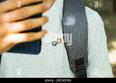 Teenager-Junge mit Autismus-Unendlichkeits-Regenbogen-Symbol mit Smartphone im Freien. Welttag des Autismus-Bewusstseins, Bewegung der Autismusrechte, Neurodiversität Stockfoto