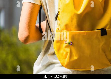 Kind mit gelbem Rucksack mit Schild mit Autismus-Unendlichkeits-Regenbogen-Symbol. Welttag des Autismus, Bewegung der Autismusrechte, Neurodiversität, Autismus Stockfoto