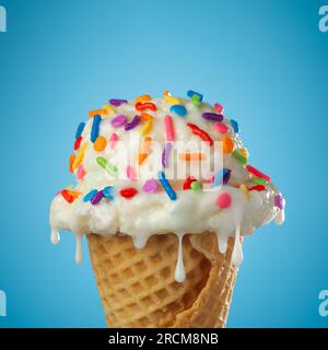 Nahaufnahme von tropfendem und schmelzendem Eis mit Vanilleeis und Waffelkonus mit bunten Streuseln auf blauem Hintergrund. Stockfoto