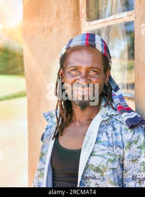 Ein Mann aus dem Rastafarianischen Dorf mit Dreadlocks, die vor dem Fenster seines Hauses stehen, ein Charakterporträt, geringe Schärfentiefe, anamorphe Linse f Stockfoto