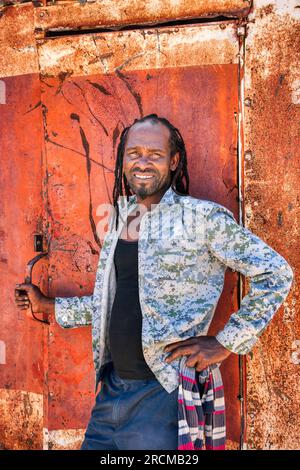 Ein junger afrikanischer Rastafarier aus dem Dorf vor der rostigen Metallhütte Stockfoto