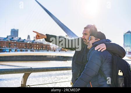 LGBT-Paar, das sich im Freien umarmt. Reisende. Einer zeigt auf einen Orientierungspunkt. Stockfoto