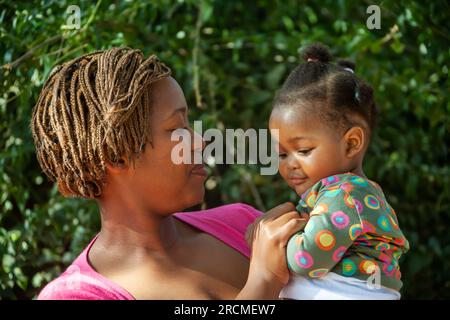 Afrikanische Mutter hält ihr Kind vor grüner Vegetation Stockfoto