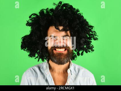 Komischer Mann mit schwarzer Perücke. Mann mit Bart und Schnurrbart in Curly Periwig. Bärtiger Hipster in schwarzer Afro-Perücke. Friseursalon. Eleganter Typ mit schwarzen Haaren Stockfoto