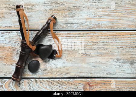 Schwarze Steinschleuder mit Steinen auf altem hellblauem Holztisch, flach liegend. Platz für Text Stockfoto