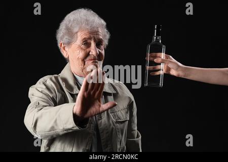 Seniorin lehnt eine Flasche Wodka auf schwarzem Hintergrund ab Stockfoto