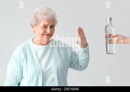 Seniorin lehnt eine Flasche Wodka auf hellem Hintergrund ab Stockfoto