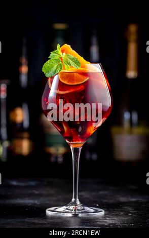 Rotes Sangria-Sommergetränk mit spanischem Rotwein, Pfirsich, Pflaume, Orange, Limette und Eis. Schwarzer Bartheke-Hintergrund, Stahlbarren und Flaschen Stockfoto