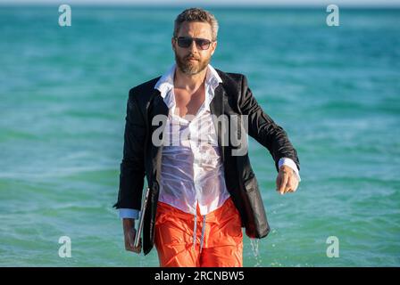 Heißer Geschäftssommer. Geschäftsführer, der das Wochenende am Strand verbringt. Geschäftsmann Chefanzug entspannen Sie sich am Strand. Geschäftsmann mit Laptop in formeller Kleidung in der Nähe von Stockfoto