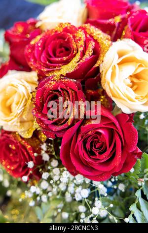 Blumenarrangements auf dem Tisch, Strauß aus roten und weißen Rosen mit goldenem Glitzer. Stockfoto