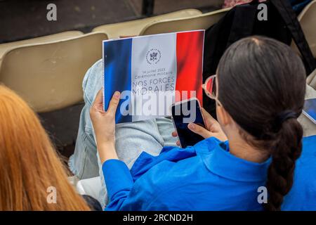 Paris, Frankreich. 14. Juli 2023. Eine Frau, die während der Parade das Buch der diesjährigen Feier mit dem Thema "Unsere moralischen Kräfte" hält. An der Zeremonie und der jährlichen Parade am 14. Juli, die den französischen Nationalfeiertag, den Bastille-Tag, auf den Champs Elysées und dem Place de la Concorde in Paris feiert, nahm der indische Premierminister Narendra Modi Teil. Dieses Jahr findet die Feier zu einer Zeit großer Proteste und sozialer Spannungen nach dem Tod eines jungen Mannes statt, der von der Polizei erschossen wurde. (Foto: Telmo Pinto/SOPA Images/Sipa USA) Guthaben: SIPA USA/Alamy Live News Stockfoto