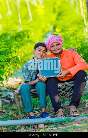 Süßes indisches Bauernkind in Schuluniform mit seinem Vater auf dem Landwirtschaftsfeld, glücklicher Vater und Sohn Stockfoto