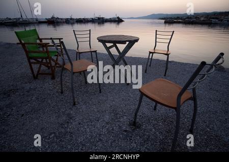 Tisch und Stühle am Hafen bei Nacht in Nea Skioni, Griechenland Stockfoto