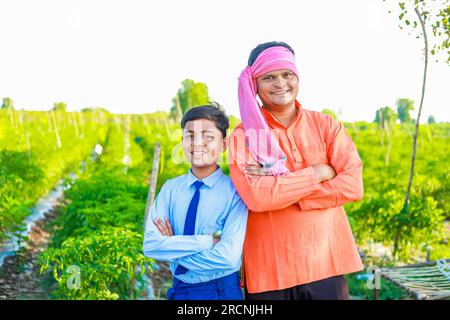 Süßes indisches Bauernkind in Schuluniform mit seinem Vater auf dem Landwirtschaftsfeld, glücklicher Vater und Sohn Stockfoto