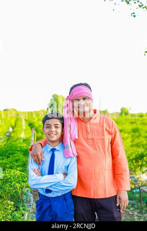 Süßes indisches Bauernkind in Schuluniform mit seinem Vater auf dem Landwirtschaftsfeld, glücklicher Vater und Sohn Stockfoto