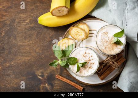 Entgiftungsmenü. Bananen-Smoothie mit Zimt in Trinkglas auf Holzhintergrund. Blick von oben. Speicherplatz kopieren. Stockfoto