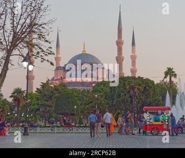 Sommerabend mit der Sultan-Ahmed-Moschee aka Blaue Moschee hinter Gärten, Touristen und einem roten Wagen, der Dekor verkauft. Istanbul, Türkei Stockfoto