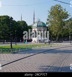 Deutscher Brunnen auf dem Sultanahmet-Platz mit der Sultan-Ahmed-Moschee aka Blaue Moschee dahinter, während die Menschen an einem Sommermorgen spazieren gehen, Istanbul, Türkei Stockfoto