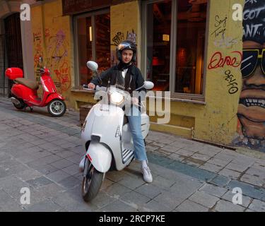 Junge Person auf einem weißen Roller mit einem roten Roller dahinter auf einer Straße mit einer gelben Mauer in Istanbul, Türkei Stockfoto