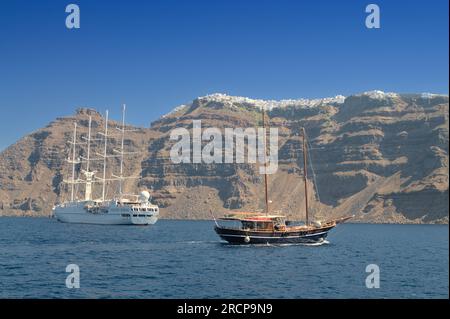 Retro-Schoner und modernes Segelschiff, das vor der felsigen Küste der Insel Santorin schwimmt. Stockfoto