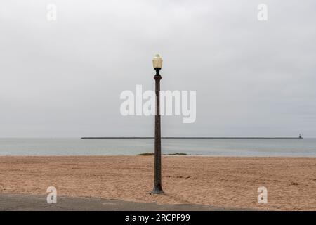 Panoramablick über den Strand des Lighthouse Point Park in New Haven, CT, USA, mit einer einzigen Straßenlaterne und Wellenbrecher in der Ferne mit historischem 1877 Building S. Stockfoto