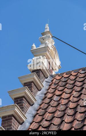 Aus einem niedrigen Winkel aus nächster Nähe sehen Sie das Dach und einen Stufensprung eines typischen Kanalhauses in den Niederlanden vor einem klaren blauen Himmel Stockfoto