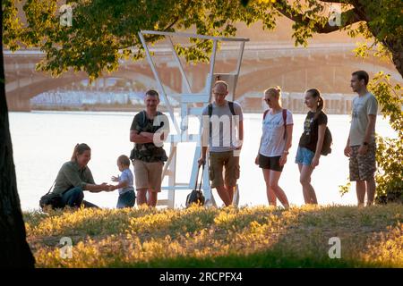 2023-07-09 Kiew, Ukraine. Freunde versammeln sich am Flussufer. Eine Gruppe von Personen genießt ihre Zeit im Park in der Nähe des Flusses Dnipro. Das Leben in Kiew während des Krieges Stockfoto