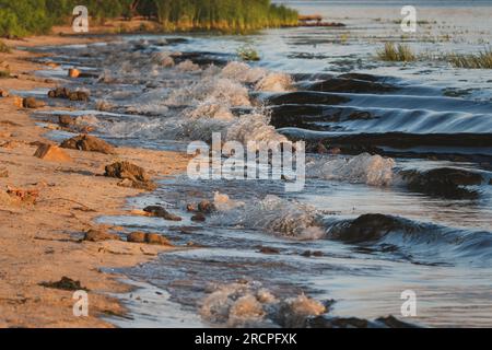 Wellen von Meeresbrunnen am Strand. Sandige Küste mit sanften Wellen am Abend. Selektiver Fokus Stockfoto