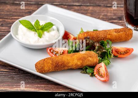 Mozzarella-Stäbchen mit Grün und Sauce auf einem weißen Porzellanteller Stockfoto