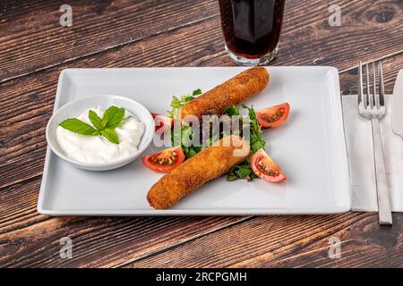 Mozzarella-Stäbchen mit Grün und Sauce auf einem weißen Porzellanteller Stockfoto