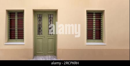 Graue, geschlossene Tür und Fenster aus Holz mit Gitter an Glas auf pinkfarbenem Wandhintergrund. Traditionelle Fassadenarchitektur mit altem Eingang. Stockfoto