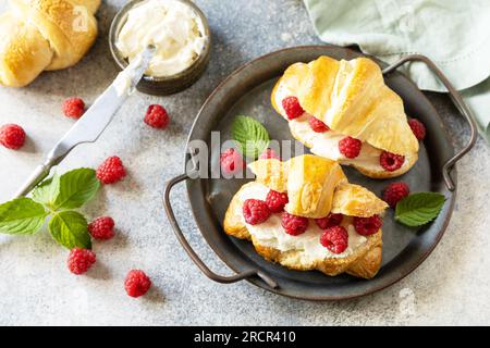 Gesundes Essen Dessertkonzept, französisches Gebäck. Leckere, frisch gebackene Croissants mit Frischkäse und Himbeere auf Steinhintergrund. Stockfoto