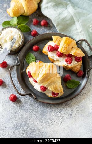 Gesundes Essen Dessertkonzept, französisches Gebäck. Leckere, frisch gebackene Croissants mit Frischkäse und Himbeere auf Steinhintergrund. Speicherplatz kopieren. Stockfoto