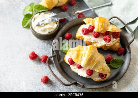 Gesundes Essen Dessertkonzept, französisches Gebäck. Leckere, frisch gebackene Croissants mit Frischkäse und Himbeere auf Steinhintergrund. Speicherplatz kopieren. Stockfoto