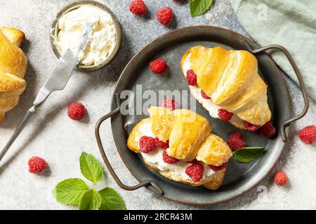 Gesundes Essen Dessertkonzept, französisches Gebäck. Leckere, frisch gebackene Croissants mit Frischkäse und Himbeere auf Steinhintergrund. Blick von oben. Stockfoto