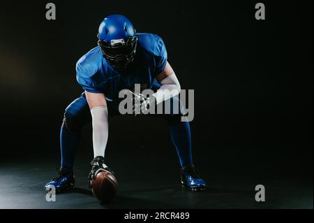Ein amerikanischer Fußballspieler ist bereit, das Spiel auf schwarzem Hintergrund zu starten. Stockfoto