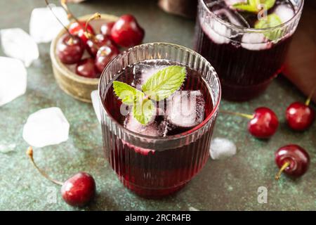 Kalte erfrischende Kirschcola in einem Glas mit Eis auf Steinhintergrund, Sommersaft. Stockfoto