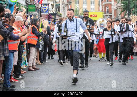 London, Großbritannien. 16. Juli 2023. Die Wettkämpfer zu Beginn des Rennens. Das jährliche Soho-Kellnerrennen durchquert Soho. Die lange Tradition, die bis in die 1950er Jahre zurückreicht, sieht Kellner aus vielen nahe gelegenen Restaurants und Bars, die mit einem Tablett, einer Serviette, einer halben Flasche Champagner und einem Champagnerglas ein Rennen durch die Straßen von Soho veranstalten. Die Kellner feiern danach. Kredit: Imageplotter/Alamy Live News Stockfoto