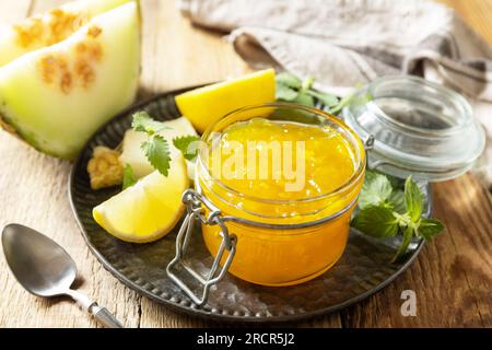 Süße Melone und Zitrusmarmelade oder Gelee in einem kleinen Glasgefäß mit frischen Melonenscheiben auf einem rustikalen Holztisch. Hausgemachtes Preserve. Stockfoto