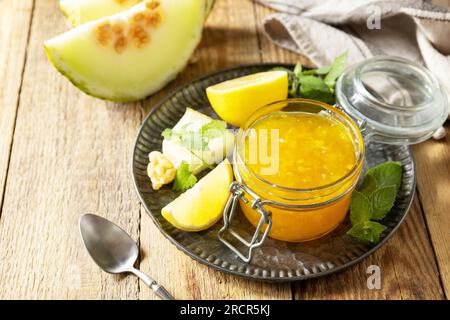 Hausgemachtes Preserve. Süße Melone und Zitrusmarmelade oder Gelee in einem kleinen Glasgefäß mit frischen Melonenscheiben auf einem rustikalen Holztisch. Speicherplatz kopieren. Stockfoto