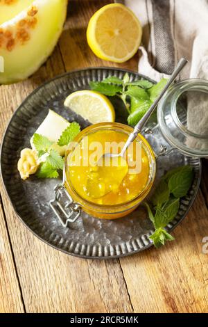 Süße Melone und Zitrusmarmelade oder Gelee in einem kleinen Glasgefäß mit frischen Melonenscheiben auf einem rustikalen Holztisch. Hausgemachtes Preserve. Speicherplatz kopieren. Stockfoto